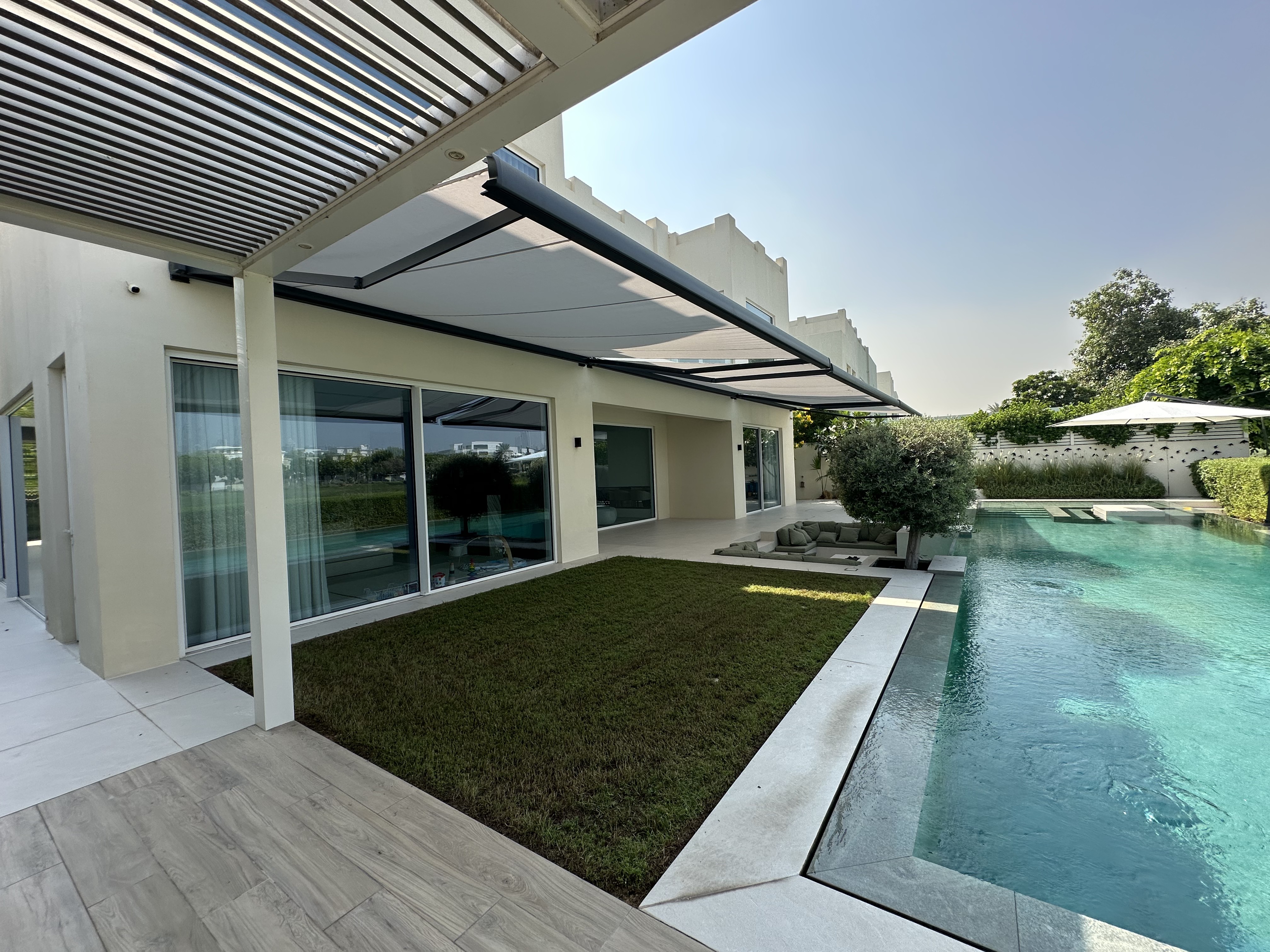 View along pool and lawn showing retractable awning extended over terrace in Meadows