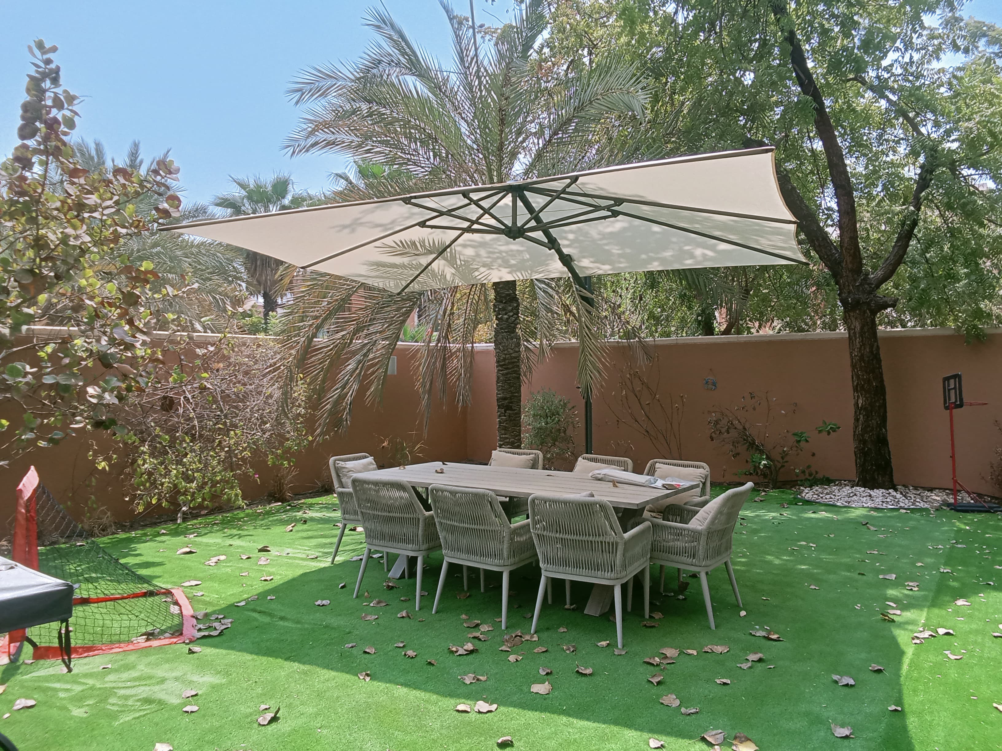Fortano umbrella opened over a rattan dining set surrounded by palm and shade trees