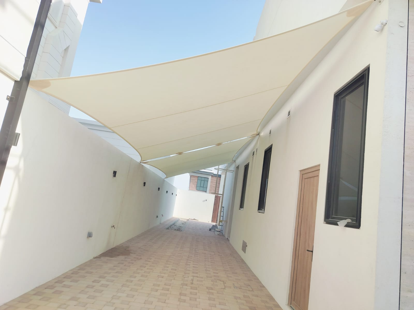 Tensioned shade sail over walkway seen from the villa entrance side with windows and door visible